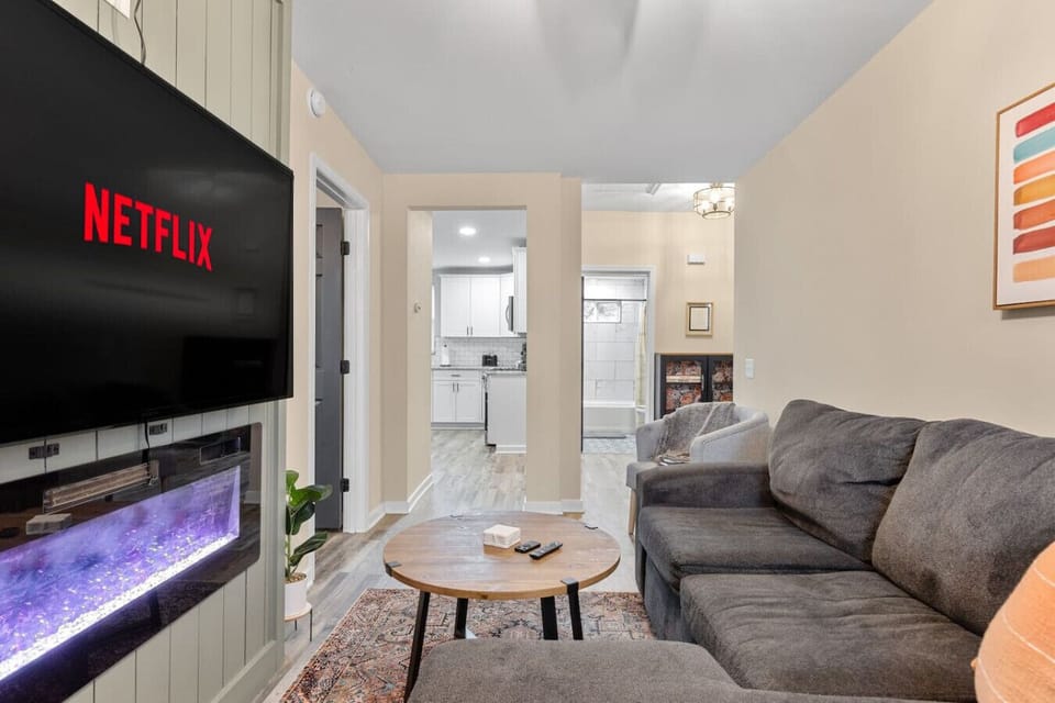 A stylish living space featuring a modern electric fireplace, plush sectional seating, and a large wall‑mounted smart TV—your intimate haven for slow mornings and cozy movie nights.