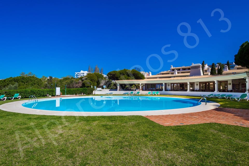 Inviting communal swimming pool at Alporchinhos resort near 813 Alporchinhos, showing the elegant curved pool design surrounded by terracotta paving, neatly trimmed hedges, and the low-rise resort buildings nestled among the green gardens of this popular Algarve holiday destination