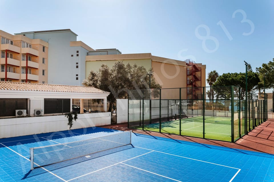 Close-up view of the Alporchinhos resort facilities near 813 Alporchinhos featuring a well-maintained tennis court in the foreground, the terracotta and white apartment buildings, communal areas, and mature trees, offering guests excellent on-site leisure amenities during their Algarve holiday