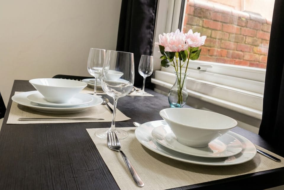 Fully set table with wine glasses and a vase of pink blooms, ready for your first meal in.