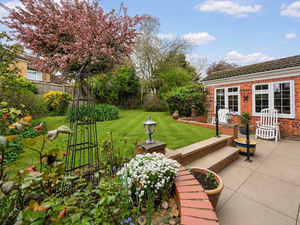 Garden: Charming patio area with raised beds bursting with white flowers, complemented by a pink blossom tree and comfor
