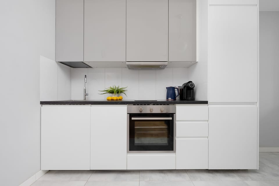A sleek kitchenette with white cabinetry and built-in appliances, including an oven and stovetop. The clean design and neutral tones give the space a modern and organized feel.