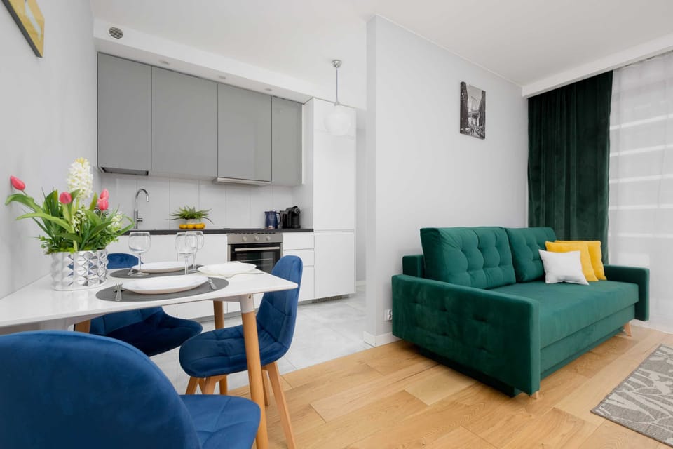 A stylish open-plan living area that combines a lounge space with a dining corner. A green sofa, a small dining table with chairs, and modern lighting fixtures create a comfortable and functional layout.