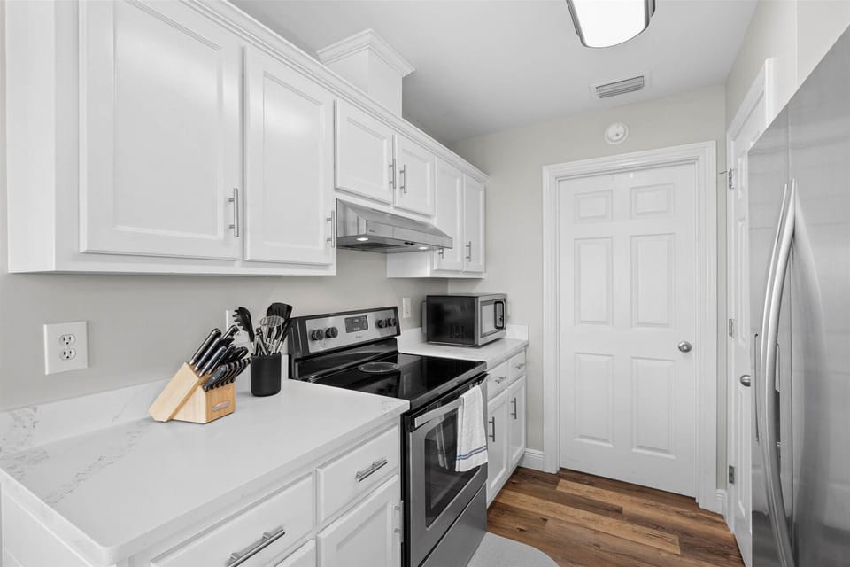 Your fully equipped kitchen awaits with pristine white cabinets, modern appliances, and all the tools you need for home cooking.