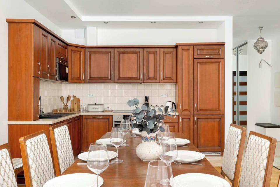 The kitchen area is designed with classic, dark wood cabinetry and integrated appliances, providing a warm and functional space for cooking. A white tablecloth covers the dining table, set and ready for a meal.