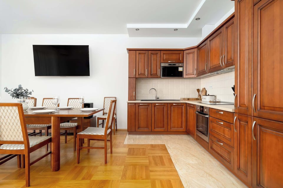 A wide view of the kitchenette reveals a U-shaped layout with ample counter space and modern built-in appliances. The dark wood contrast beautifully with the light-colored countertops and backsplash.