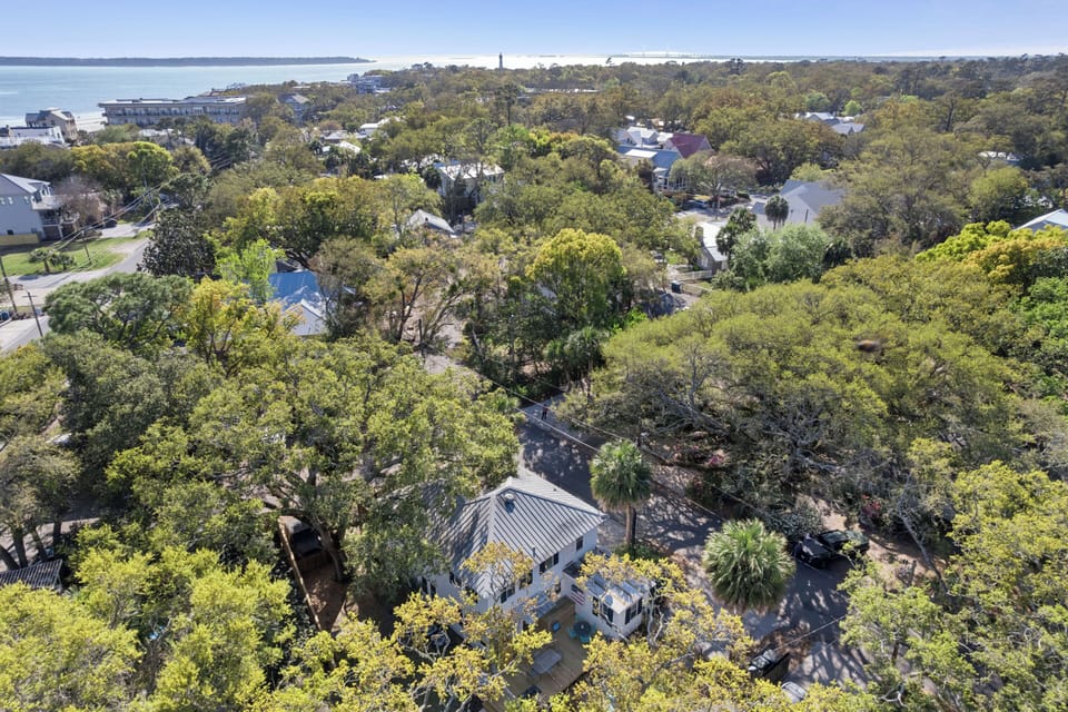 Aerial view of coastal property nestled among mature trees with nearby beach access and charming neighborhood surroundings.
