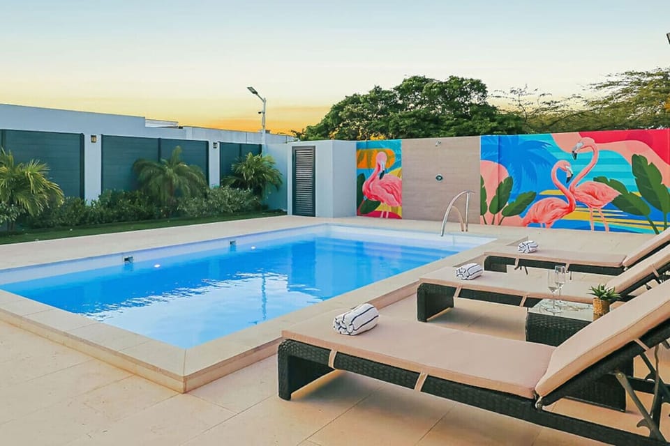Relax by the sparkling private pool on comfortable sun loungers, surrounded by lush greenery and vibrant tropical murals—your own slice of paradise.