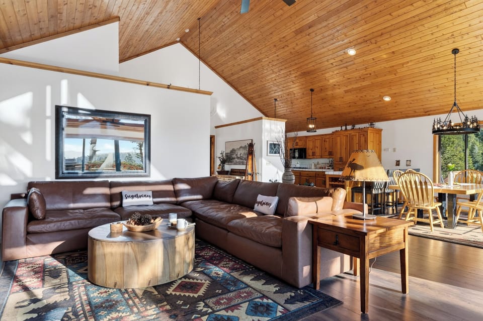 Spacious cabin living and dining area with vaulted wood ceilings, cozy leather seating, and nature‑filled views.