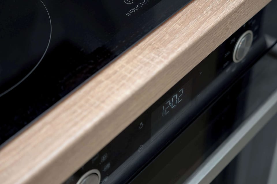An extreme close-up focuses on the edge of a light wood countertop and the digital display of a kitchen appliance. The sleek black finish of the control panel suggests a modern induction or electric stovetop.