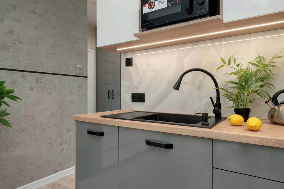 A detailed shot of the kitchen corner highlights a black sink with a high-arc faucet set into a wooden counter. A small potted plant and two lemons add a pop of color to the grey workspace.