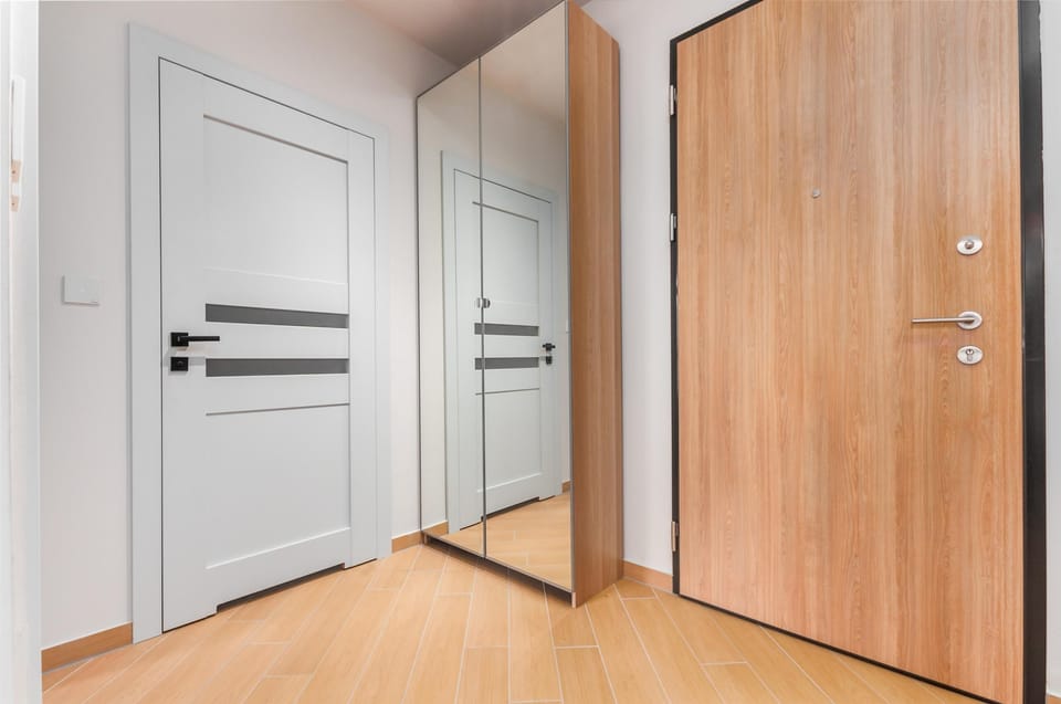 The entrance area features a white door, a mirrored closet, and a light wood-finish door. The space is bright and functional, serving as a clean transition into the home.