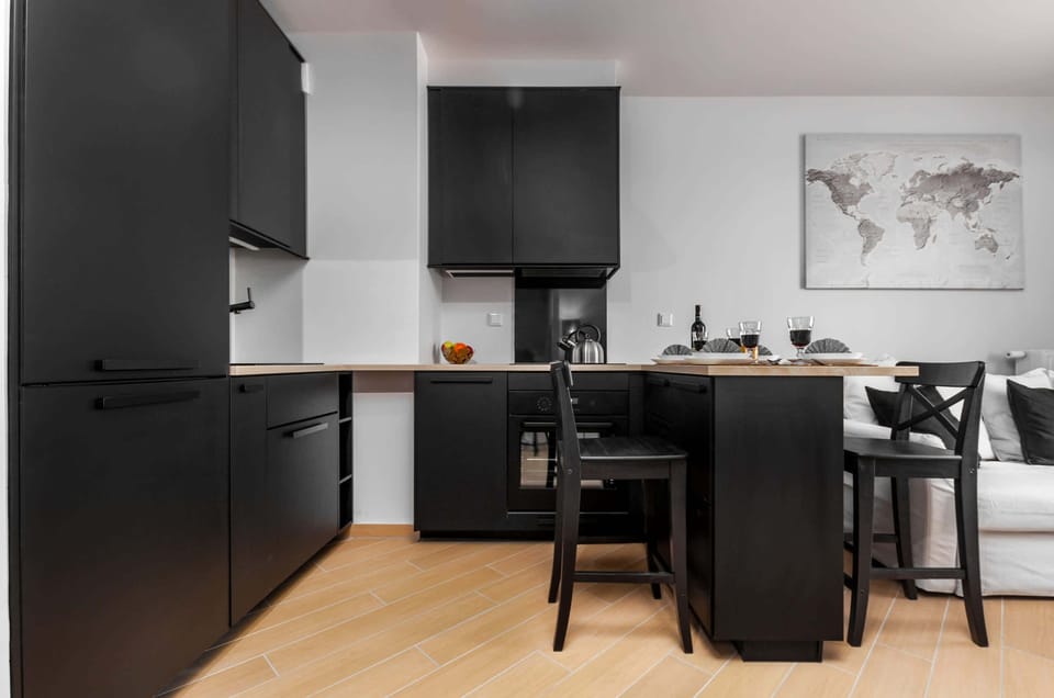 This perspective shows the full kitchenette layout with its matte black finish and integrated appliances. The wooden countertops add warmth to the dark, contemporary design.