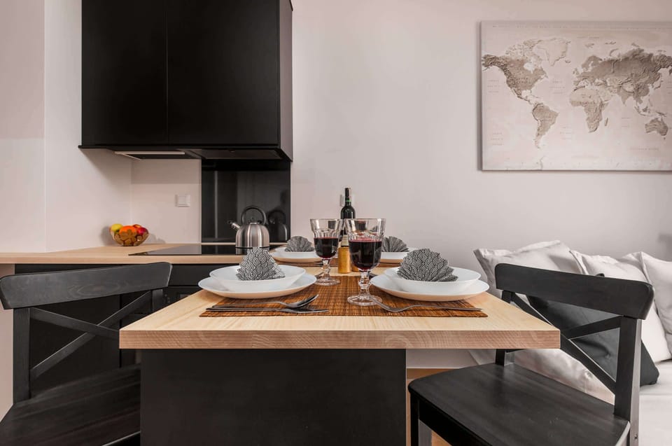 A kitchen island with a light wood top is set with formal place settings and black chairs. Modern black cabinets are visible in the background, providing a sharp contrast.