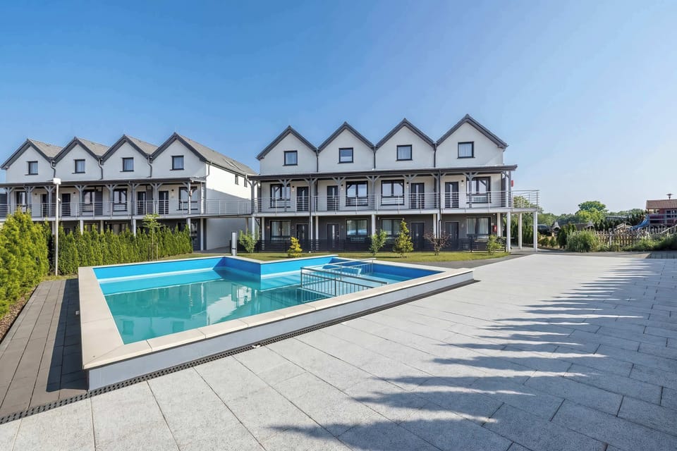 A communal outdoor area features a sparkling blue swimming pool surrounded by a paved terrace and modern duplex buildings.