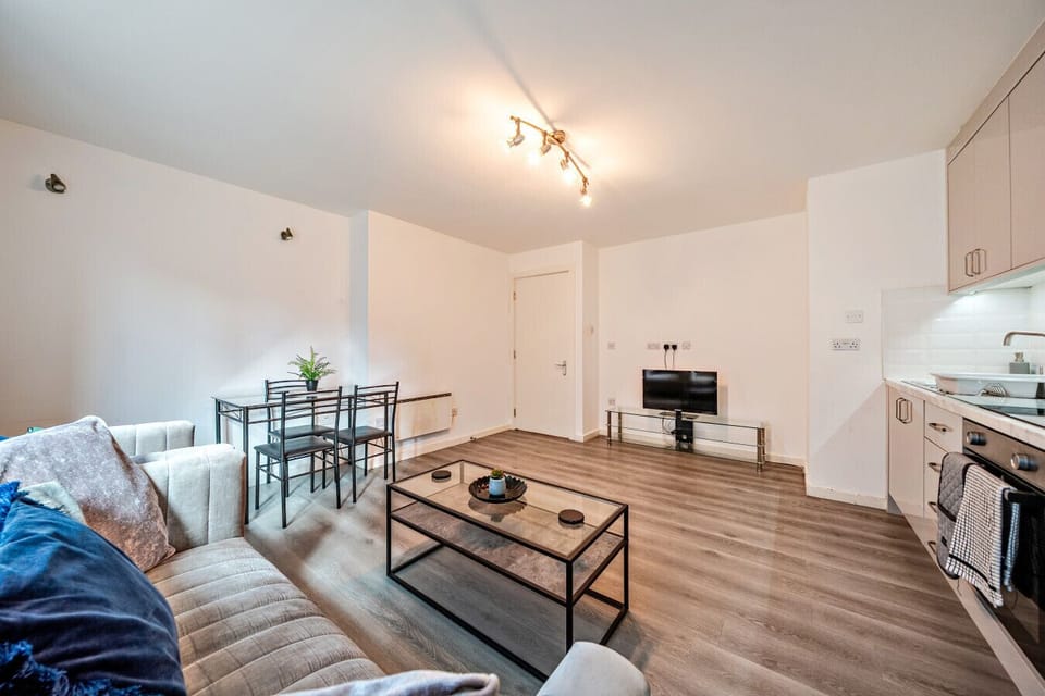 Living and dining area with a sofa, glass dining table with four chairs, coffee table, and TV on a stand.