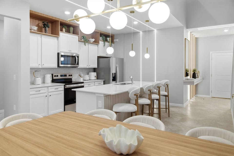 Enjoy the bright, airy kitchen with sleek white cabinetry and elegant pendant lighting. Stylish bar stools invite casual dining, while the warm wood dining table adds a cozy touch to this modern culinary space.