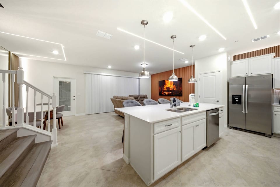 This spacious kitchen boasts a large island and sleek white cabinetry, perfect for meal prep or casual dining. Warm wood accents and modern stainless steel appliances create a welcoming atmosphere for your culinary adventures.