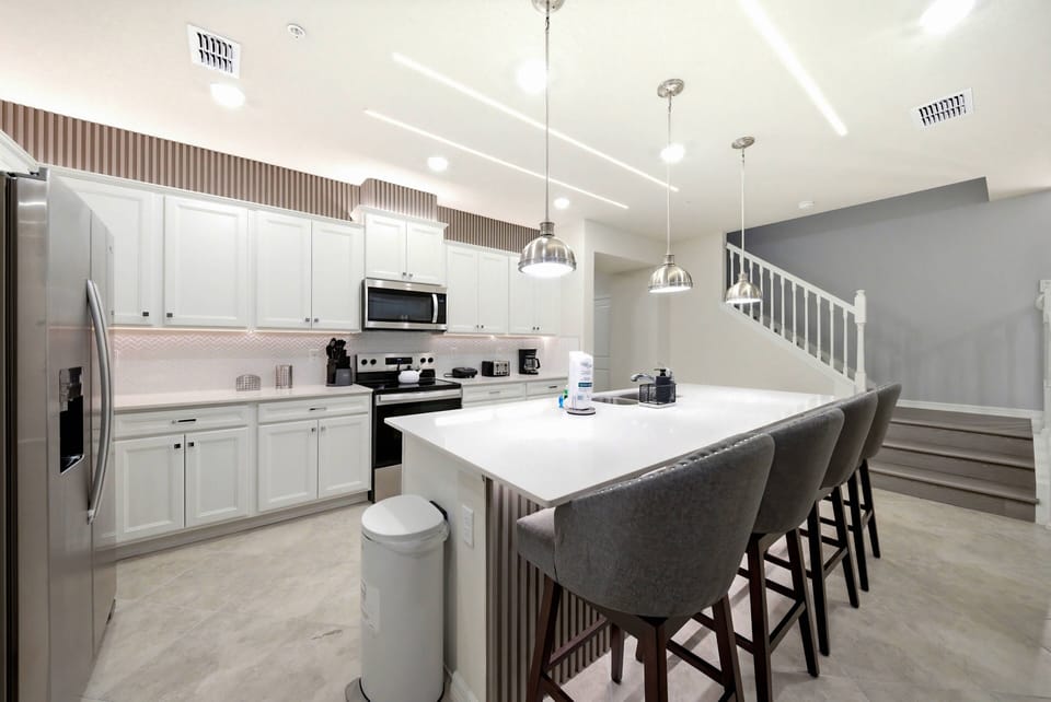 Enjoy a bright, modern kitchen featuring sleek white cabinetry and a spacious island with stylish bar stools, perfect for casual dining. The warm lighting creates an inviting atmosphere, ideal for all your culinary adventures.