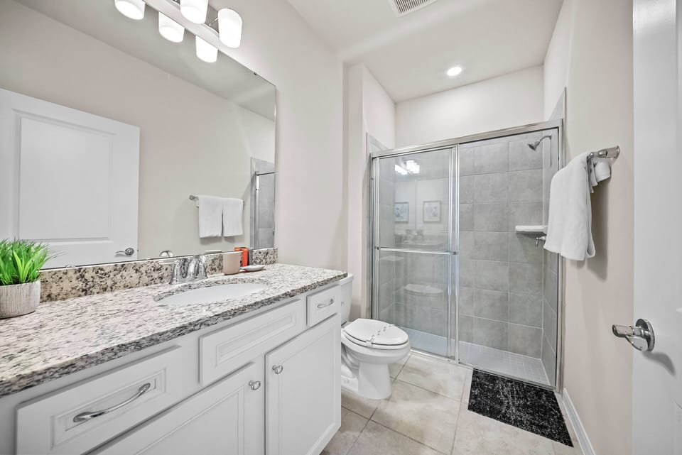 Experience a beautifully designed bathroom with elegant granite countertops and a spacious glass shower, creating a relaxing atmosphere. Bright lighting enhances the airy feel, making it the perfect space to unwind and rejuvenate.