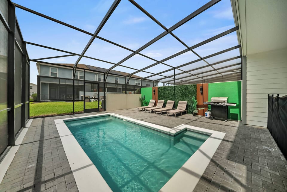 Discover your private oasis featuring a sparkling pool and stylish loungers within a bright, screened-in enclosure. The sleek tile flooring and lush greenery enhance this refreshing retreat, perfect for relaxation.