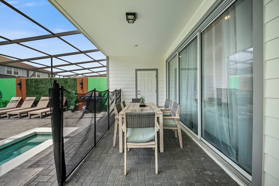 Enjoy al fresco dining on the stylish, weathered wood table set against a backdrop of sleek glass doors. The inviting outdoor area features comfortable lounge chairs, perfect for soaking up the sun by the pool.