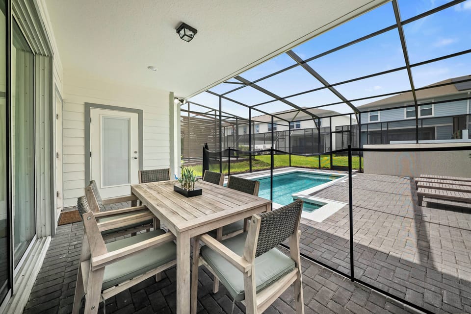 Step outside to a lovely patio featuring a stylish wooden dining table and comfy gray chairs. Enjoy the fresh air and sunshine as you gather around, with a sparkling pool nearby, perfect for a relaxing day.
