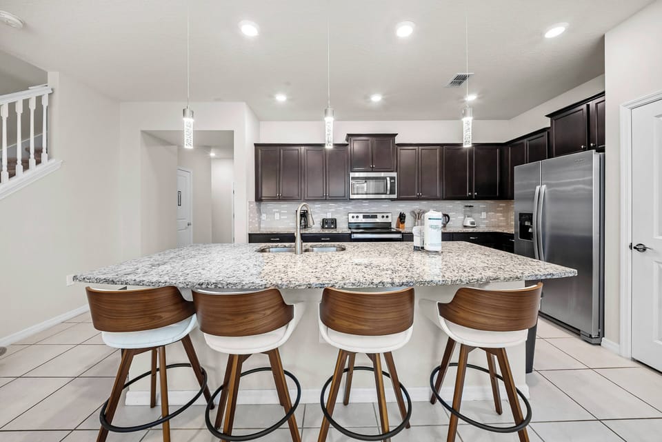 This stylish kitchen inspires your culinary creativity with spacious dark wood cabinets and a gleaming granite countertop. Enjoy casual meals at the chic bar seating, beautifully lit by modern pendant lights for a warm atmosphere.