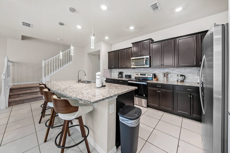 Experience a stylish kitchen with warm wood cabinets and granite countertops, ideal for casual dining at the inviting bar. Bright lighting sets the mood as you create culinary delights with modern appliances.