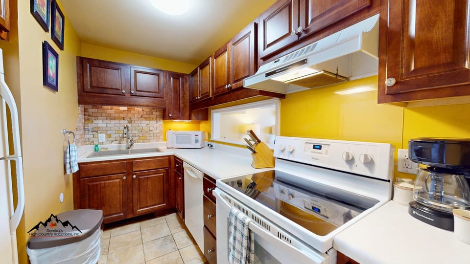 Your fully equipped kitchen features rich wood cabinets, modern appliances, and cheerful yellow walls that create a warm cooking space.