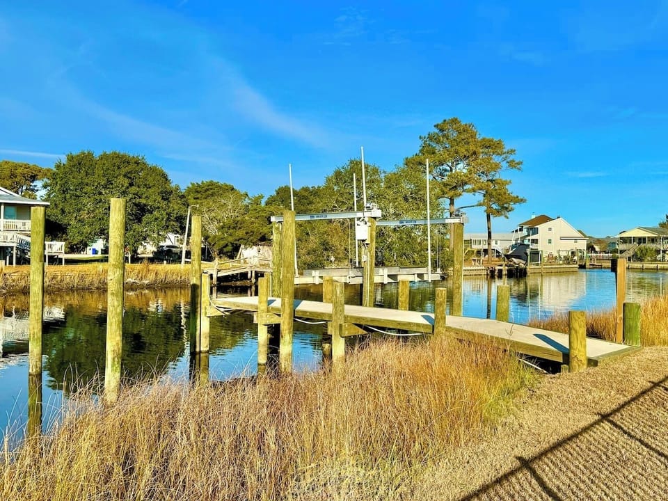 Private backyard dock with boat lift and fillet table, fenced-in backyard, fire pit with Adirondack chairs, hammocks, propane grill, picnic table, outdoor shower, expansive waterfront back deck with table and seating, neighborhood boat ramp and dock