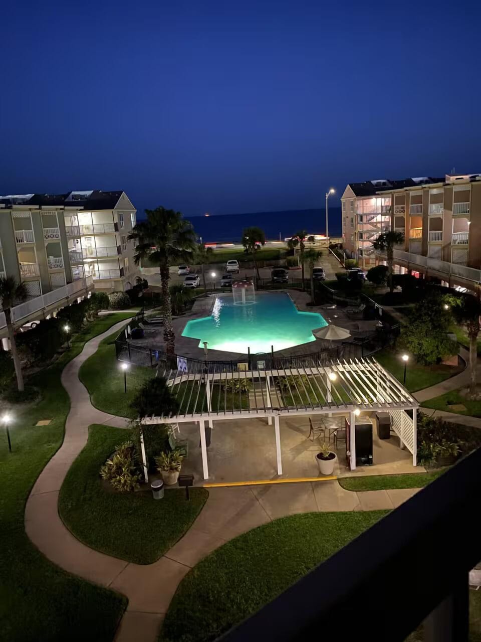 Nighttime pool views with landscaped grounds and a glimpse of the ocean