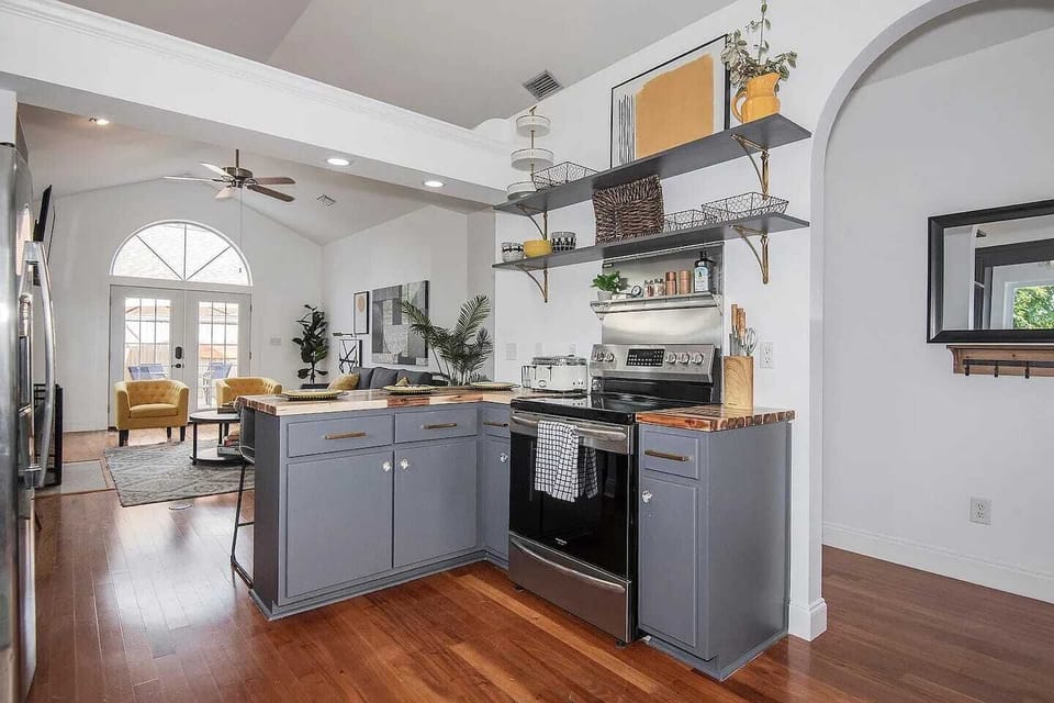 Cook, sip, and connect in this beautifully styled kitchen featuring butcher block countertops, sleek open shelving, and stainless steel appliances. Fully stocked with cookware, spices, and a coffee station this kitchen invites both quick breakfasts a