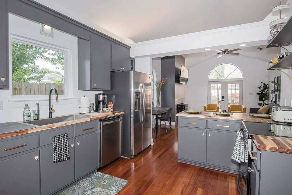 Cook with ease in this stylish kitchen featuring butcher block counters, stainless steel appliances, a coffee station, and a peek into the bright, cozy living room. Ideal for staying connected while prepping meals.