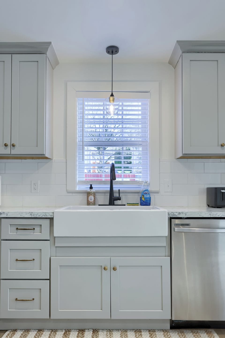 Bright modern kitchen with farmhouse sink, subway tile, and stainless dishwasher