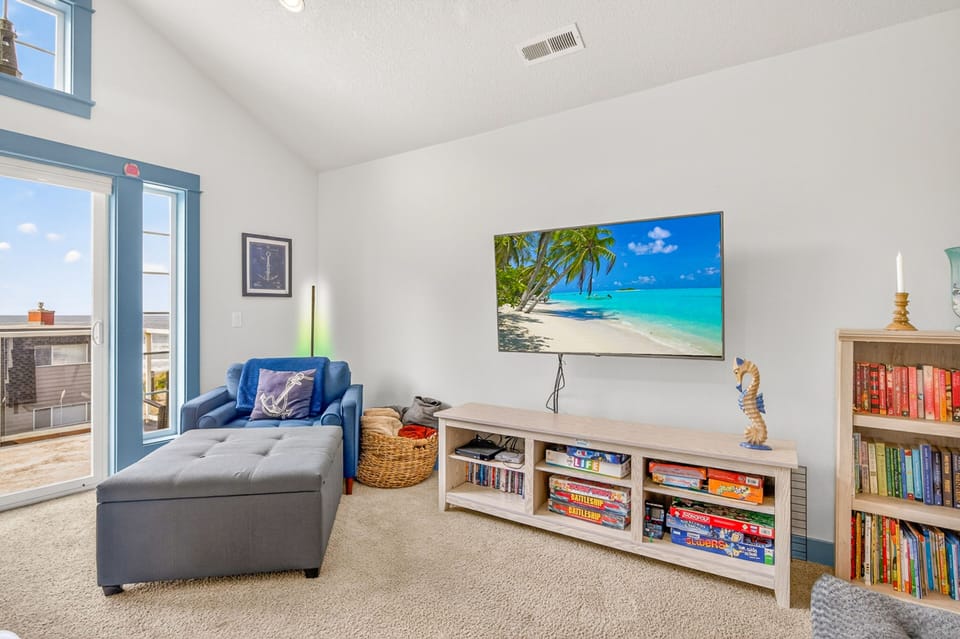 Unwind in your bright living space with plush seating, tropical beach views on the big screen, and shelves stocked with books and games for cozy evenings in.