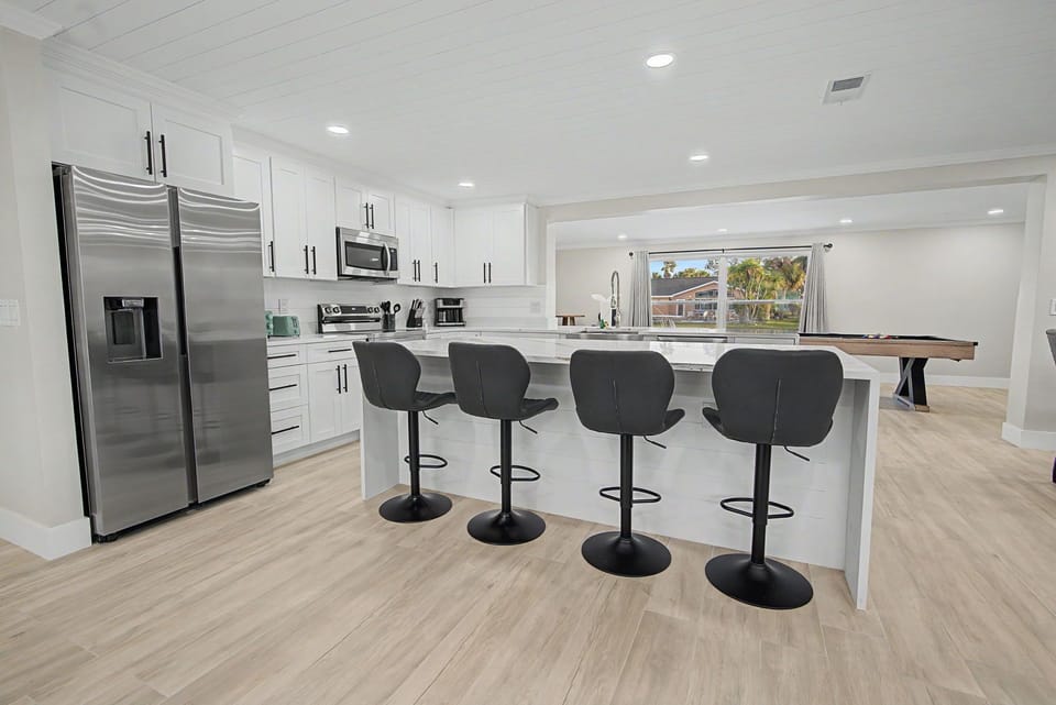 Your modern kitchen features sleek white cabinets, stainless steel appliances, and a spacious island with seating for four—perfect for morning coffee or casual meals.