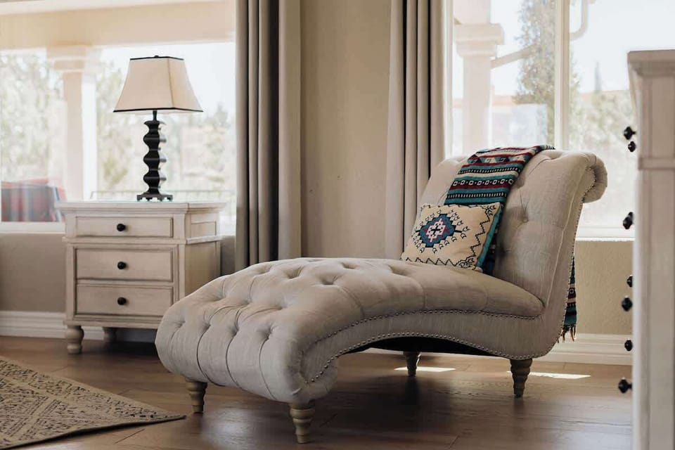 Sink into this elegant tufted chaise lounge where you can unwind with a book in natural light streaming through soft curtains.
