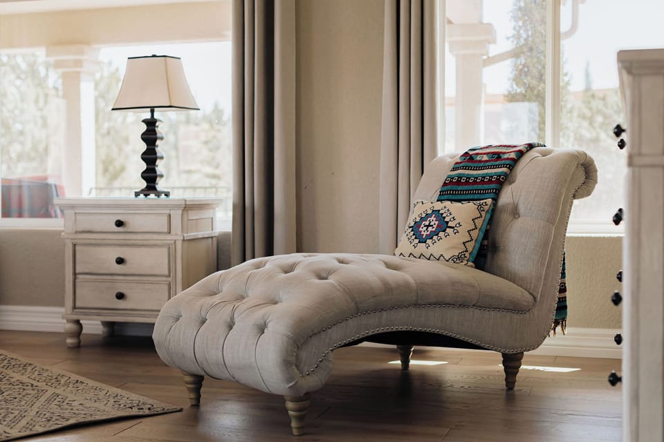 Sink into this elegant tufted chaise lounge where you can unwind with a book in natural light streaming through soft curtains.