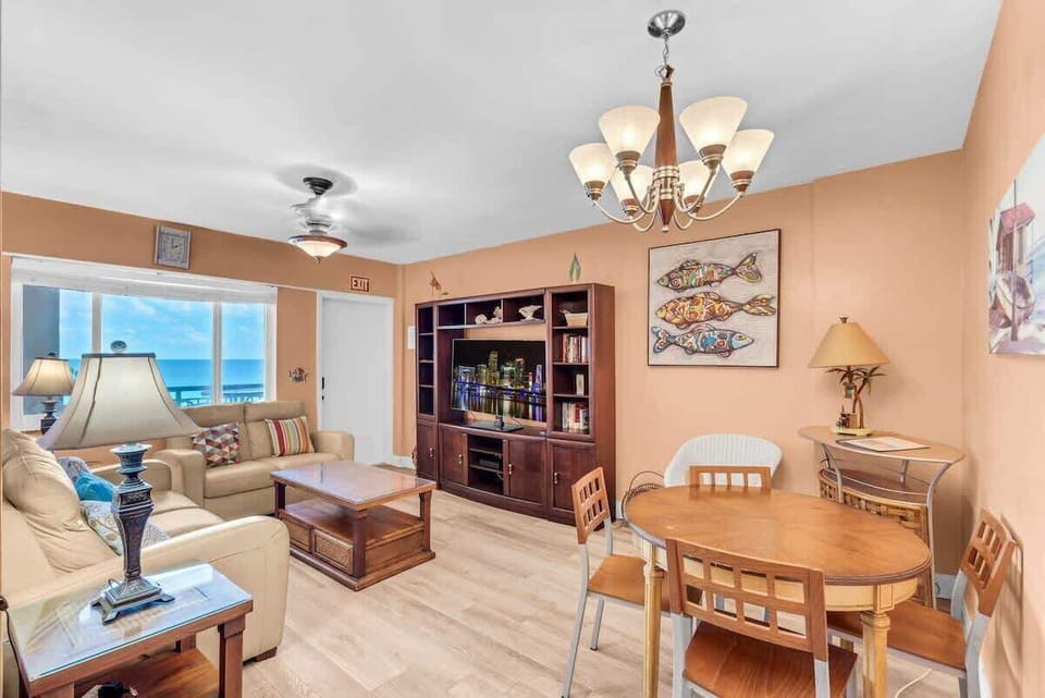 Open-plan living and dining with ocean views right through the window. Leather sofas, a wood entertainment center with flat-screen TV, and dining for four — all in one comfortable, breezy space.