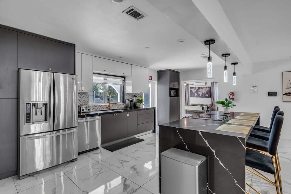 Cook like a pro in our fully equipped gourmet kitchen — premium stainless appliances, black marble island, gold bar seating, chevron backsplash & floor-to-ceiling cabinetry. Pure luxury! 