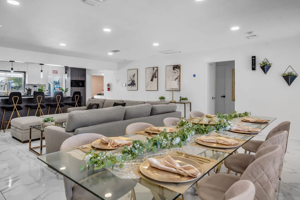 Entertain in style! Our elegantly set glass dining table for 10 with gold chargers & floral garland flows into a chic living area and gourmet kitchen — perfect for special celebrations! 