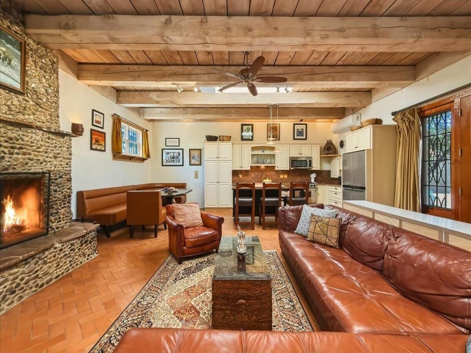 An open, loft-style layout brings together the living room, dining nook, and kitchen, with a wood-burning fireplace and warm wood beams throughout.