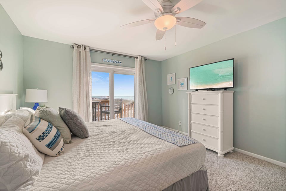 Wall-mounted flat-screen TV and a sliding door to the dune-front deck. The king master at The Gathering Place is hard to leave.