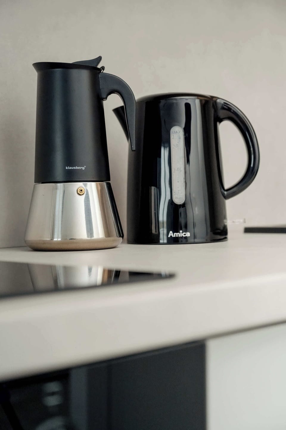 A close-up focuses on a black electric kettle and a French press sitting on a white countertop. This shot emphasizes the modern kitchen accessories available in the home.