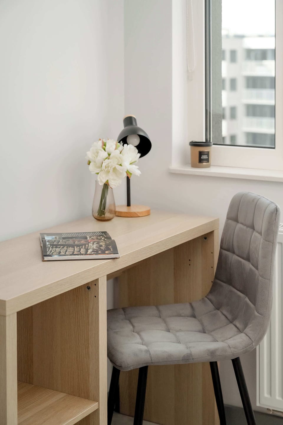 A dedicated workspace features a light wood desk paired with a comfortable grey chair. A small lamp and a decorative plant create an inviting atmosphere for productivity.