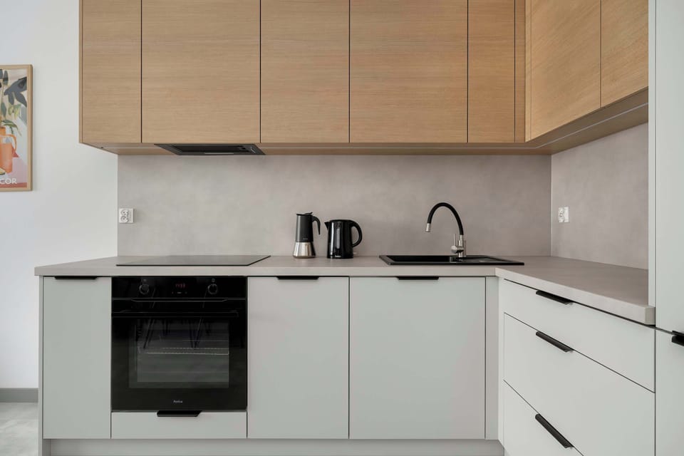 A contemporary kitchen displays white cabinetry contrasted by warm wood-toned upper cupboards. Integrated appliances like an oven and stovetop provide a clean, functional look.