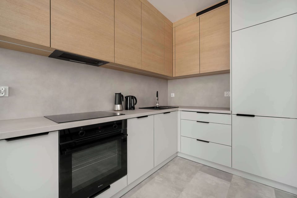Modern kitchen cabinetry is shown from an angle, highlighting the built-in stovetop and oven. The mix of wood and white finishes creates a balanced, scandinavian-inspired aesthetic.