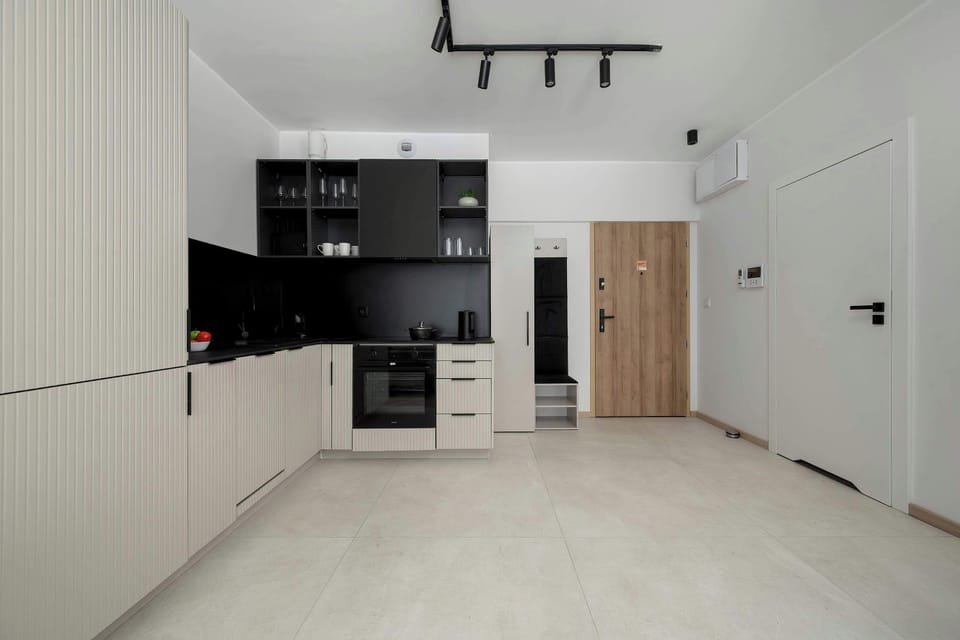 A modern kitchenette with white cabinetry and a contrasting black backsplash, creating a sleek and elegant look. Built-in appliances and clean lines give the space a functional, minimalist feel.