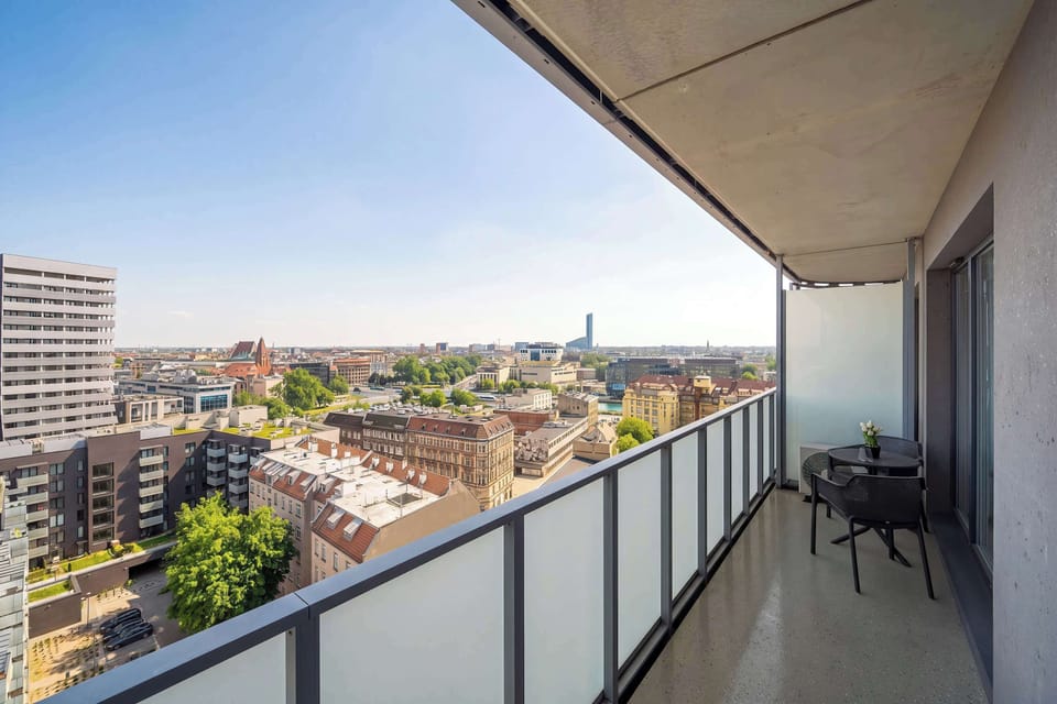 A long balcony with a glass railing offering a panoramic city view. The space is narrow but ideal for enjoying fresh air and relaxing outdoors.